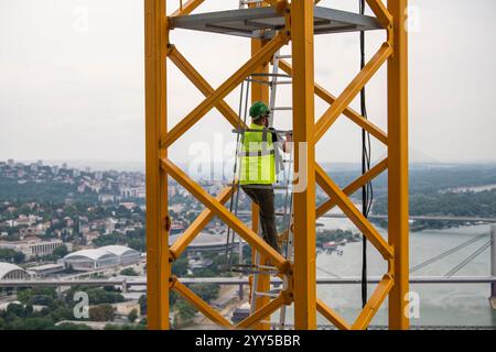 L'operatore della gru sale su una scala in acciaio giallo, una scala di accesso con gru. Cantiere di grattacielo a grattacielo. Foto Stock