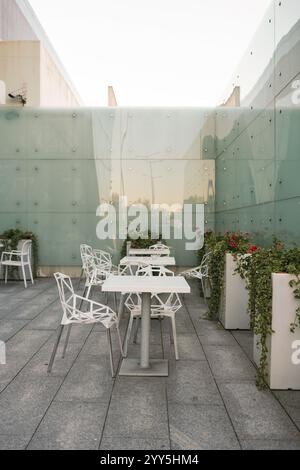 Accogliente area salotto esterna con sedie e tavolo bianchi rustici, mobili da patio, circondata da pareti in vetro, punto relax, arredamento rustico moderno. Foto Stock