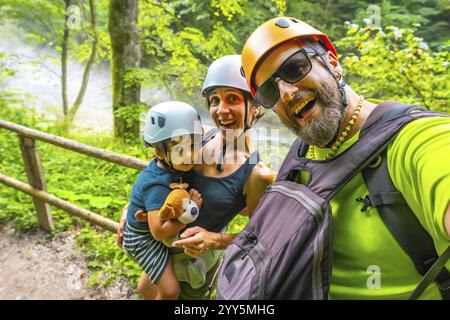 Famiglia felice che indossa i caschi per un selfie mentre fai un'escursione su un sentiero vicino a un fiume nella gola di vintgar, Bled, slovenia Foto Stock