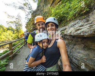 La famiglia indossa caschi che scattano selfie mentre cammina su una passerella in legno accanto alla parete di roccia nella splendida gola di vintgar vicino a Bled, in slovenia Foto Stock