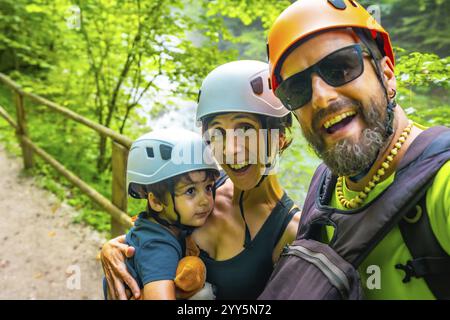 Famiglia felice che indossa caschi, scattando un selfie alla gola di vintgar, una passerella di legno a Bled, slovenia Foto Stock