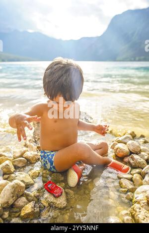 Bambini piccoli che si godono le vacanze estive, giocando con un'auto giocattolo sulle rive del lago di bohinj in slovenia Foto Stock