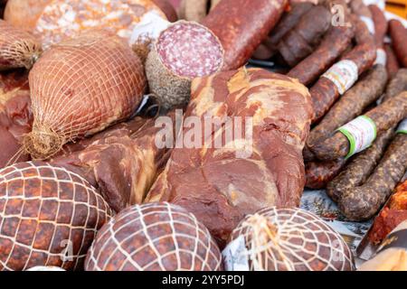 Una collezione di affettati splendidamente disposti, con vari tipi di salumi, tra cui salame e prosciutto, esposti su un tavolo in un mercatino di Natale. Le calde tonalità seppia esaltano l'atmosfera festosa. Foto Stock