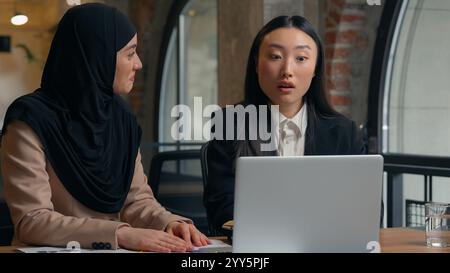Donne multirazziali colleghi d'affari donne d'affari multietniche ragazze coreane asiatiche lavoratrici manager musulmane in hijab insieme lavoro laptop shock Foto Stock