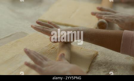 Famiglia a casa cucina due persone mani braccia femminili primo piano donna irriconoscibile che insegna bambino figlia bambino ragazza impastare l'impasto utilizzare il mattarello Foto Stock