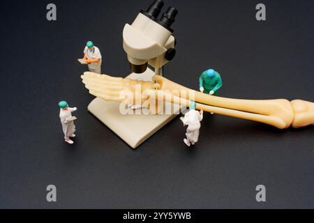 Modello di scheletro del piede umano posizionato sotto un microscopio con medici in miniatura che lo esaminano, collocato su uno sfondo scuro per scopi educativi. Foto Stock