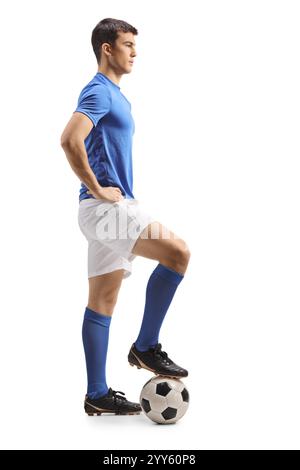 Giocatore di calcio con la maglia blu e pantaloncini bianchi in piedi con il piede su una palla isolata su sfondo bianco Foto Stock