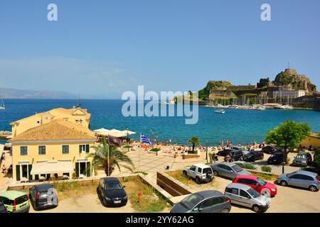 Corfù, Grecia - 6 giugno 2024. Un bar e una spiaggia cittadina sul Mar Ionio vicino alla zona di porto della città di Corfù. Patrimonio dell'umanità dell'UNESCO, la Fortezza Vecchia Foto Stock