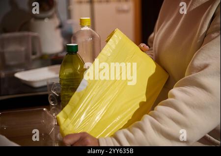 Un individuo in un ambiente domestico di cucina gestisce articoli riciclabili, tra cui plastica e involucri. L'immagine trasmette consapevolezza ambientale, s Foto Stock