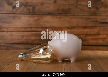 Salvadanaio e lampadina su un tavolo di legno. Concetto di risparmio energetico Foto Stock