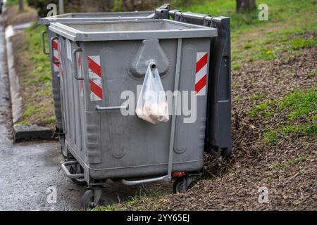 Un sacchetto di plastica bianco con il pane, appendi il cassonetto di rifiuti metallici (contenitore), lasciato per senzatetto poveri e affamati in città Foto Stock