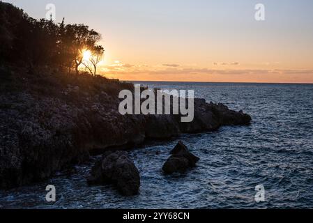 Tramonto sulla costa marina con scogliere rocciose. Riva del mare vicino a una montagna con rocce e piccole onde. Primo piano di roccia di pietra in acque cristalline. Foto Stock