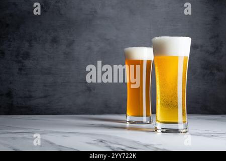 Due bicchieri alti di Golden Yellow Blonde e pale Ale Beer con grandi teste di schiuma deliziose e uno sfondo grigio Foto Stock