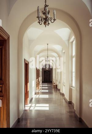 Corridoio ad arco beige con pavimento piastrellato in un edificio del XIX secolo. La luce del sole splende dai finestrini sul lato destro. Foto Stock