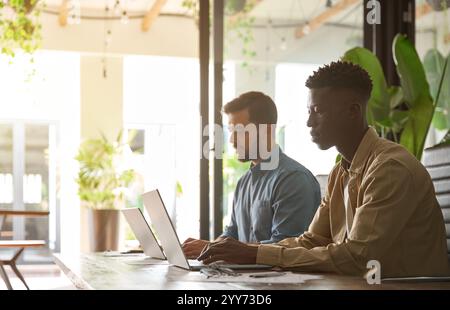 Team di due uomini d'affari impegnati che lavorano in ufficio utilizzando computer portatili. Foto Stock