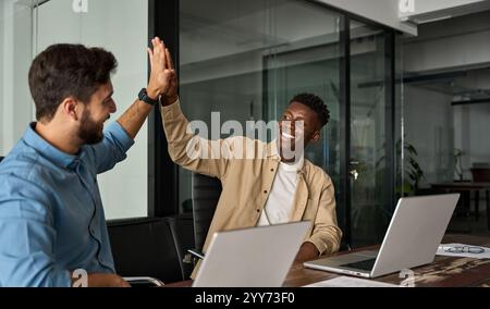 Giovani uomini d'affari felici e diversi che danno cinque voti per celebrare il raggiungimento degli obiettivi. Foto Stock