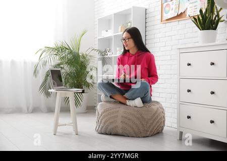 Grafica asiatica femminile che lavora con tablet su pouf in ufficio Foto Stock