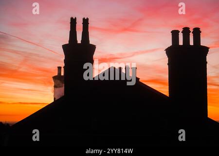 Londra, Regno Unito. 20 dicembre 2024 . Caminetti e un tetto residenziale a Wimbledon, a sud ovest di Londra, si stagliano contro un cielo di fuoco colorato all'alba in una fredda mattina ghiacciata. Credit.Amer Ghazzal/Alamy Live News Foto Stock