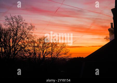 Londra, Regno Unito. 20 dicembre 2024 . Caminetti e un tetto residenziale a Wimbledon, a sud ovest di Londra, si stagliano contro un cielo di fuoco colorato all'alba in una fredda mattina ghiacciata. Credit.Amer Ghazzal/Alamy Live News Foto Stock