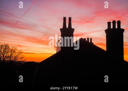 Londra, Regno Unito. 20 dicembre 2024 . Caminetti e un tetto residenziale a Wimbledon, a sud ovest di Londra, si stagliano contro un cielo di fuoco colorato all'alba in una fredda mattina ghiacciata. Credit.Amer Ghazzal/Alamy Live News Foto Stock