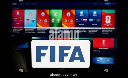 In questa immagine, una persona ha in mano un cellulare con il logo della Federazione Internazionale di calcio (FIFA) davanti alla pagina web. Foto Stock