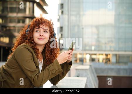 La donna ascolta la musica con le cuffie e tiene il telefono in strada Foto Stock