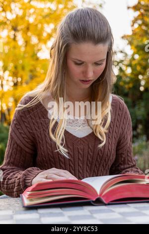 Una giovane donna si è concentrata sulla lettura di un libro all'aperto in autunno Foto Stock