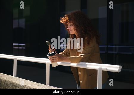 Donna d'affari che si gode una pausa caffè, usa il telefono e sorride Foto Stock