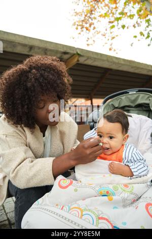 Mamma che dà da mangiare al bambino nel passeggino all'aperto Foto Stock