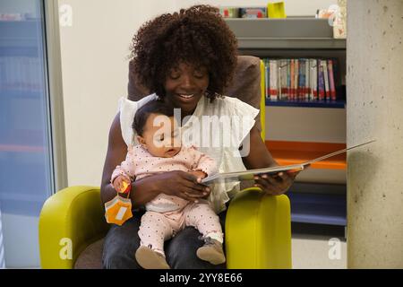 Madre che legge un libro alla sua bambina in biblioteca Foto Stock