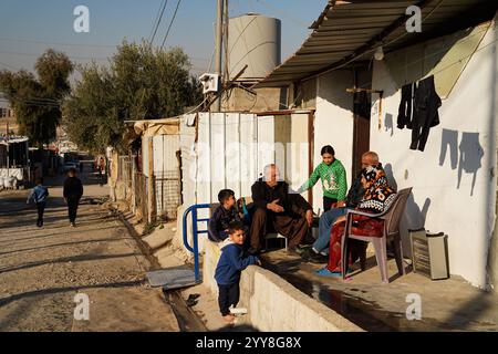 La gente si trova di fronte alla casa del campo di Domiz per i rifugiati curdi siriani a circa 18 km a sud-ovest della città di Duhok nella regione del Kurdistan. La provincia di Duhok ospita 92.000 rifugiati siriani su 275.000 rifugiati nella regione del Kurdistan in Iraq che sono migrati dallo scoppio della rivoluzione siriana nel 2011. La maggior parte di loro si rifiuta di tornare nel loro paese nonostante la caduta del regime di Bashar al-Assad per paura dello scoppio di conflitti armati tra le forze democratiche siriane (SDF) e l'esercito nazionale siriano sostenuto dai turchi o con Hayat Tahrir al-Sham e altre forze di opposizione che lo hanno fatto Foto Stock