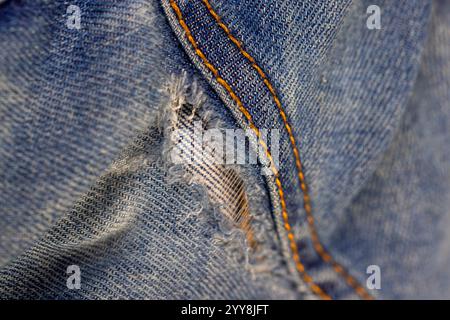 dettagli di vecchi jeans strappati da usura frequente, jeans danneggiati con un foro nel tessuto adatto per la riparazione e cuciture Foto Stock