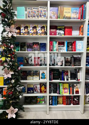 Kiev, Ucraina - 18 dicembre 2024: Libreria splendidamente organizzata accanto a un albero di Natale, con vari libri colorati e creatina Foto Stock