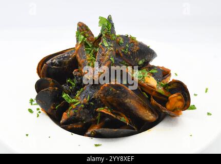 Cozze cotte in padella con prezzemolo su sfondo bianco. Foto Stock