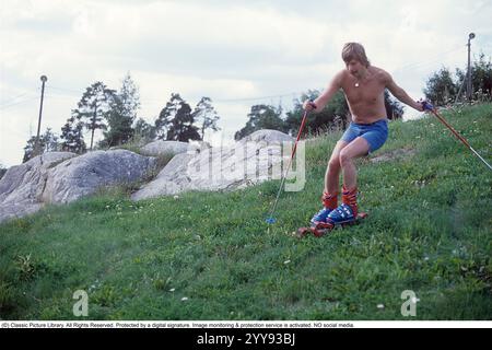 Slalom senza neve. Nel 1980 una nuova invenzione degli sci d'erba è in fase di sperimentazione, in estate. Gli sci sono costruiti con nastri rotanti e hanno funzionalità simili a quelle degli sci normali. Nella foto un uomo che prova gli sci rotolanti in estate su una collina ricoperta di erba. C'erano una manciata di produttori di sci d'erba negli anni '1980 Ecco una pagina web che racconta la storia dello sci d'erba: https://www.theskijournal.com/exclusive/grassholes/ rif. DV25 Foto Stock