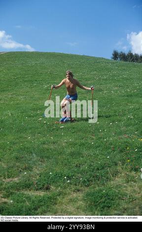 Slalom senza neve. Nel 1980 una nuova invenzione degli sci d'erba è in fase di sperimentazione, in estate. Gli sci sono costruiti con nastri rotanti e hanno funzionalità simili a quelle degli sci normali. Nella foto un uomo che prova gli sci rotolanti in estate su una collina ricoperta di erba. C'erano una manciata di produttori di sci d'erba negli anni '1980 Ecco una pagina web che racconta la storia dello sci d'erba: https://www.theskijournal.com/exclusive/grassholes/ rif. DV25 Foto Stock