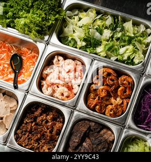 Un vivace buffet con una varietà di ingredienti freschi, tra cui gamberi grigliati e cotti, carni marinate, lattuga fresca e verdure Foto Stock