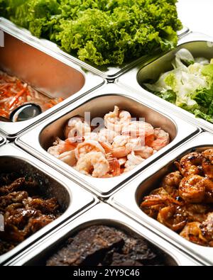 Un vivace buffet con una varietà di ingredienti freschi, tra cui gamberi grigliati e cotti, carni marinate, lattuga fresca e verdure Foto Stock