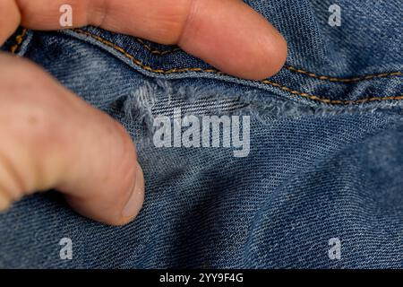 vecchi jeans strappati da usura frequente, jeans danneggiati con un foro nel tessuto adatto per la riparazione e le cuciture da vicino Foto Stock