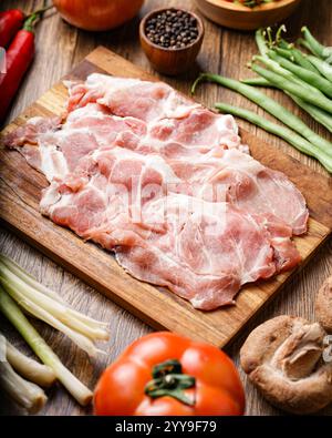 Spalla di maiale tagliata di fresco disposta su una tavola rustica di legno, circondata da verdure e spezie vivaci, pronta per un sostanzioso pasto casalingo. Foto Stock