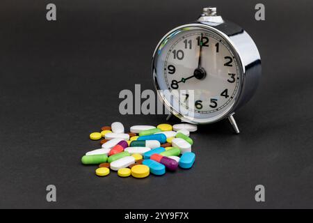 Pillole medicinali con sveglia su sfondo nero Foto Stock