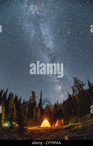 Scena notturna mozzafiato della via Lattea con stelle sul monte Assiniboine con tenda illuminata in campeggio nella foresta autunnale del parco provinciale, British Co Foto Stock