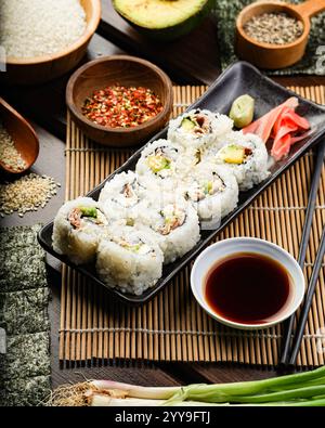 Un piatto di sushi ben organizzato con ripieni di avocado e frutti di mare, servito con salsa di soia, wasabi e zenzero sottaceto su un bambù Foto Stock