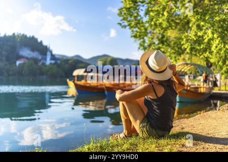 Giovane donna con un cappello di paglia seduto sul lago dissanguato, ammirando le tradizionali barche pletna con l'assunzione della chiesa di maria in vista Foto Stock