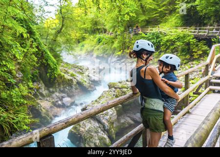 Madre che tiene in braccio suo figlio mentre si gode la vista mozzafiato del turchese fiume radovna che scorre attraverso la gola di vintgar vicino a Bled, in slovenia Foto Stock