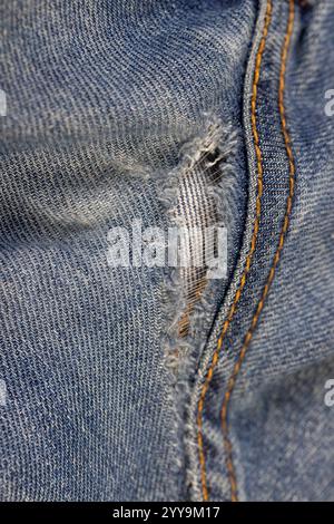 dettagli di vecchi jeans strappati da usura frequente, jeans danneggiati con un foro nel tessuto adatto per la riparazione e cuciture Foto Stock