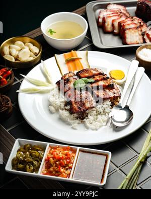 Carne di maiale siu alla griglia in stile cinese servita su riso bianco al vapore con uova sode, verdure fresche, salse assortite Foto Stock
