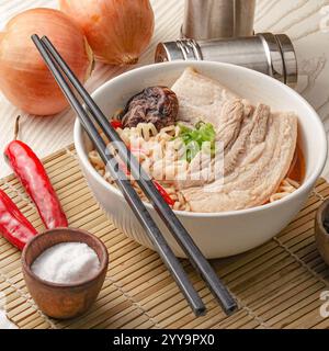 Primo piano di una ciotola di ramen con spesse fette di pancia di maiale bollita, cipolle verdi e spaghetti in un ricco brodo saporito. Foto Stock