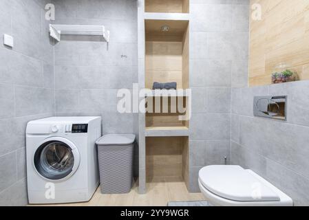 Bagno pulito ed elegante con lavatrice, WC e ripiani in legno per offrire utilità multifunzionale in una struttura ben organizzata Foto Stock