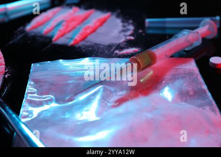 Tossicodipendenza. Sacchetto di plastica con polvere e siringa su tavolo nero con luci al neon, primo piano Foto Stock